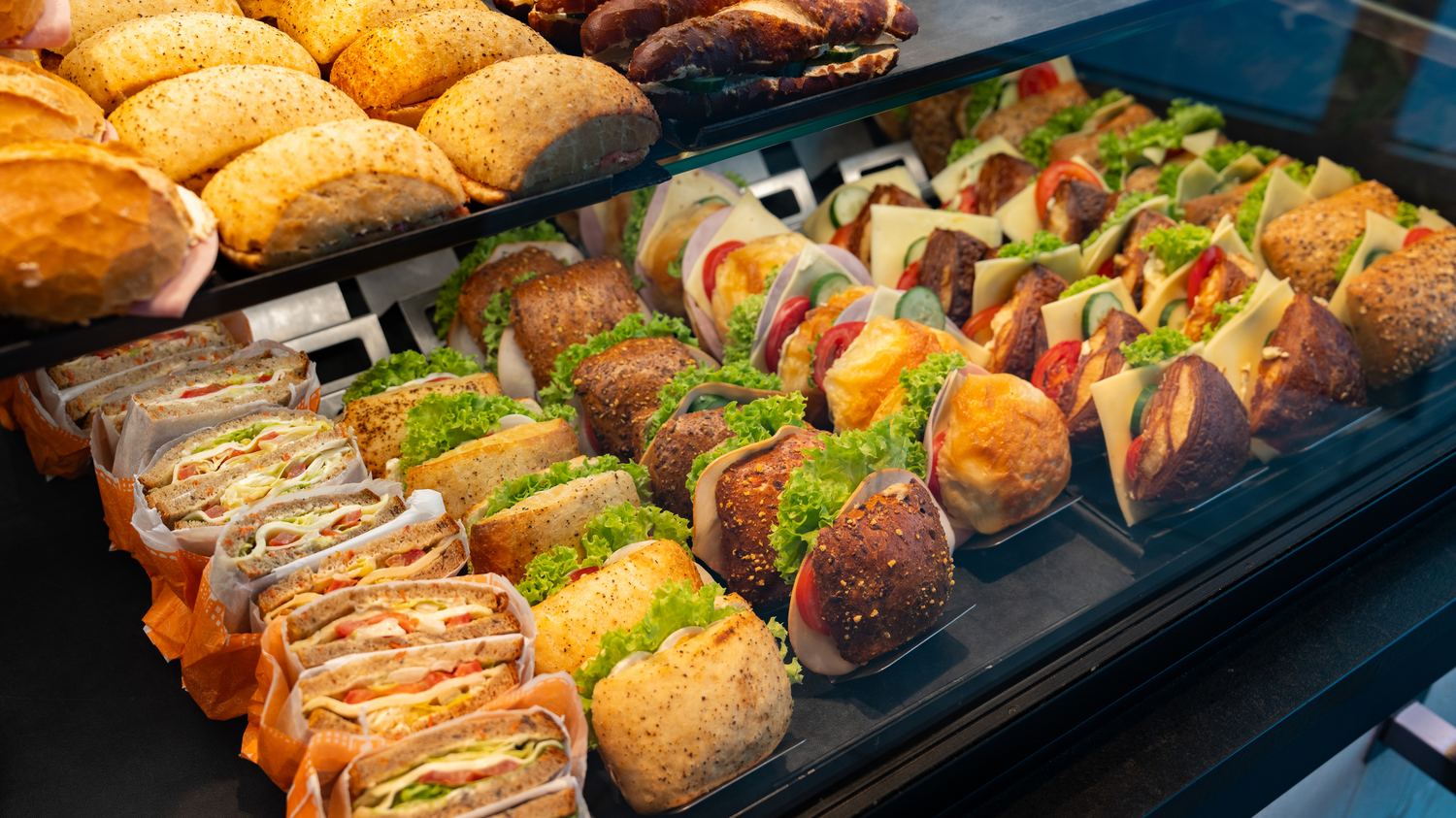 Auslage einer Bäckerei mit belegten Brötchen, Laugenstangen und Sandwiches.