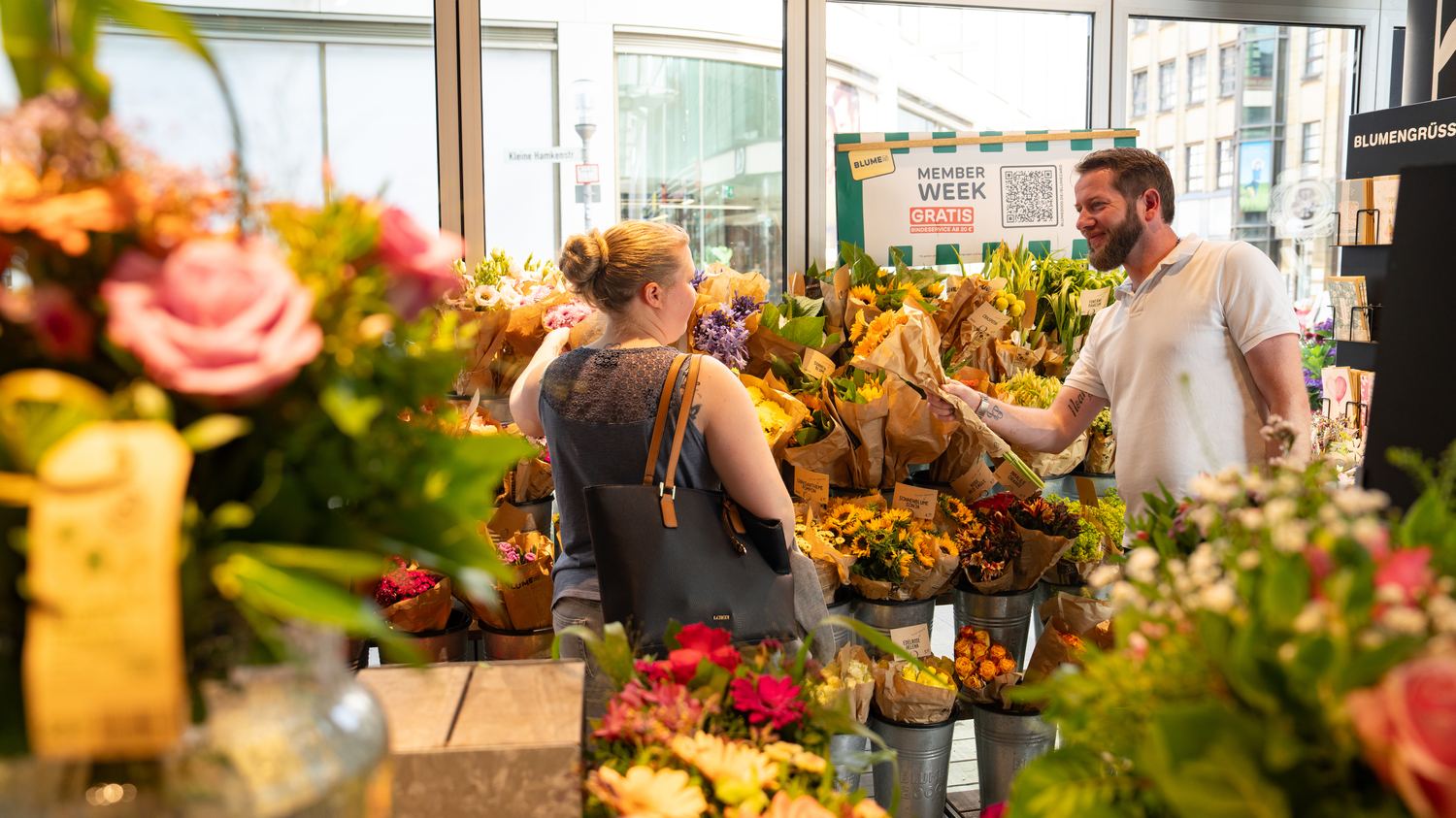 Eine Frau und ein Verkäufer stellen im Blumenladen einen bunten Strauß zusammen.