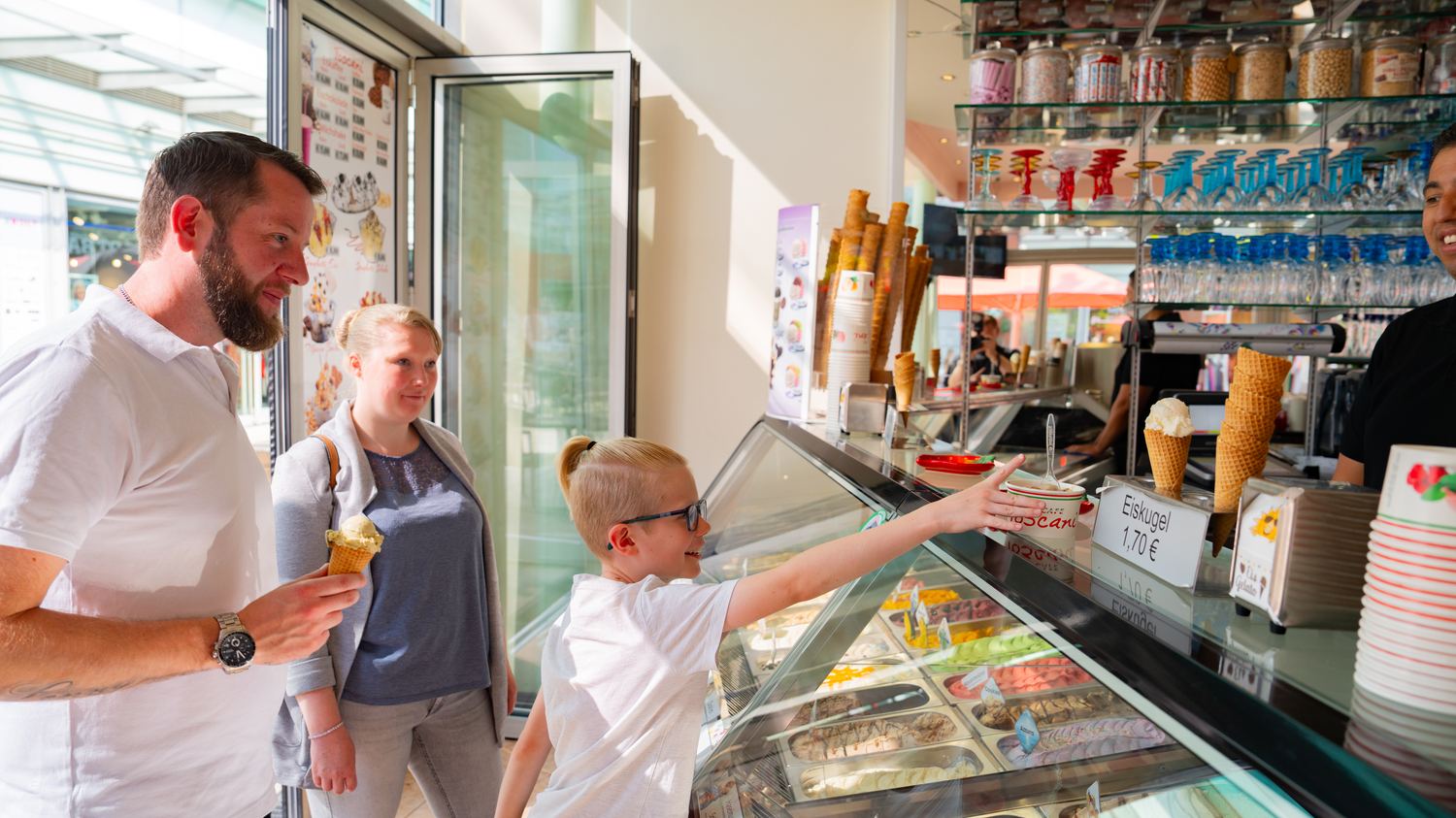Ein Junge zeigt an der Theke eines Eiscafés auf eine Eissorte.